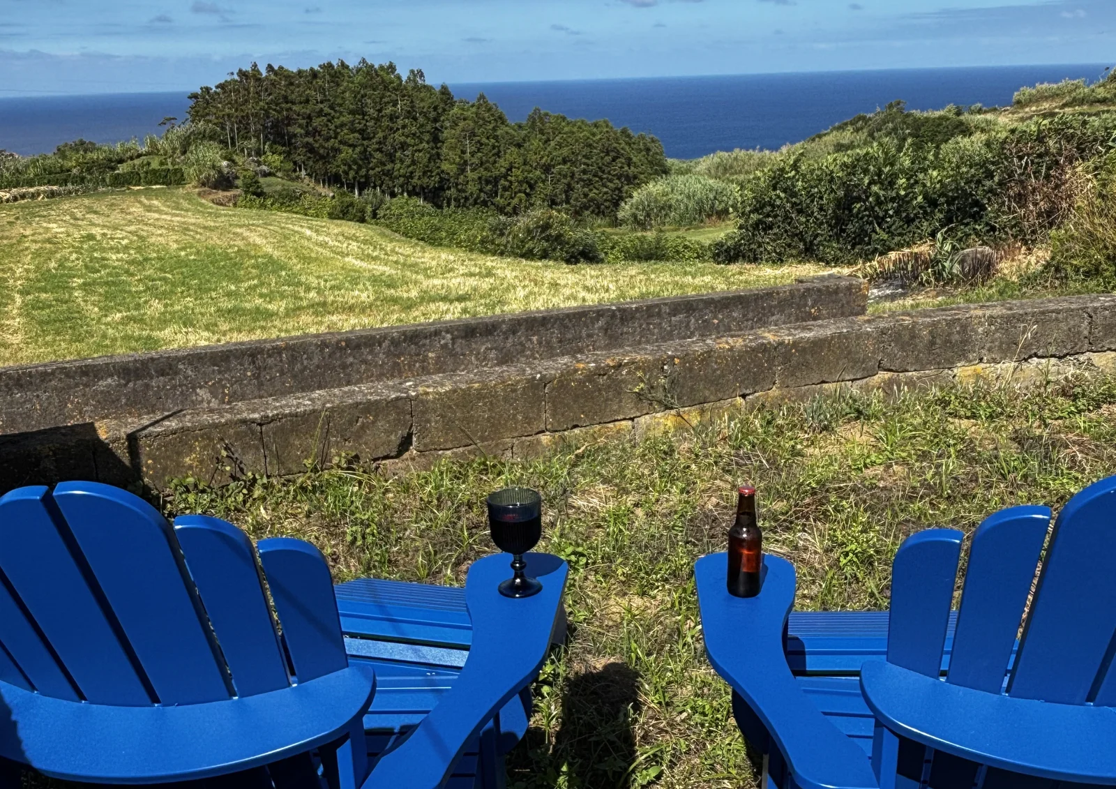 Cadeiras azuis no jardim da Casa das Brisas Matinais, com campos e mar ao fundo.