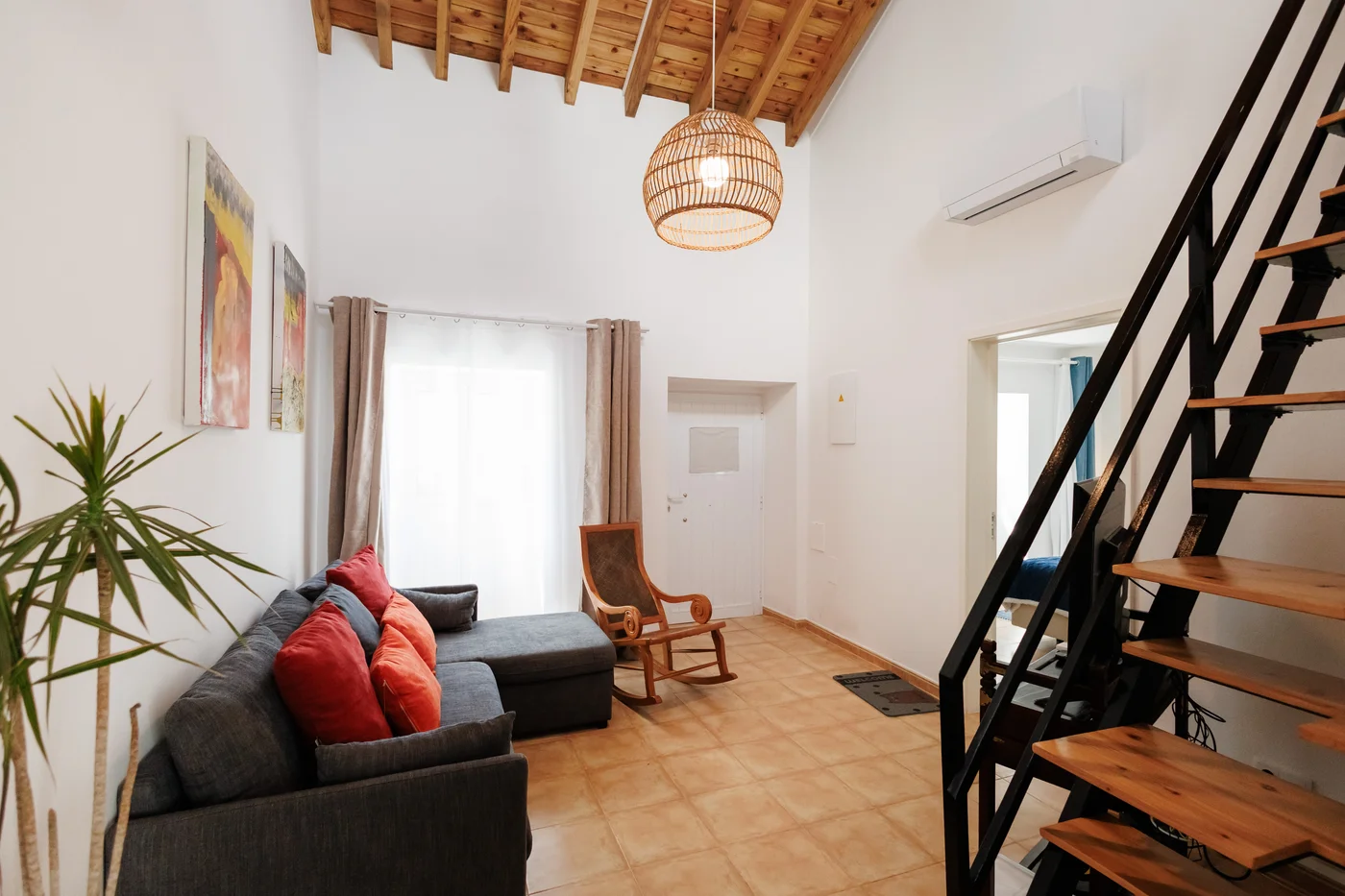 Holiday rental living room with a sofa, wooden chair and stairs to the upper floor.